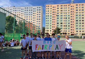Uczniowie w strojach sportowych trzymające bilbord z napisem Fair Play